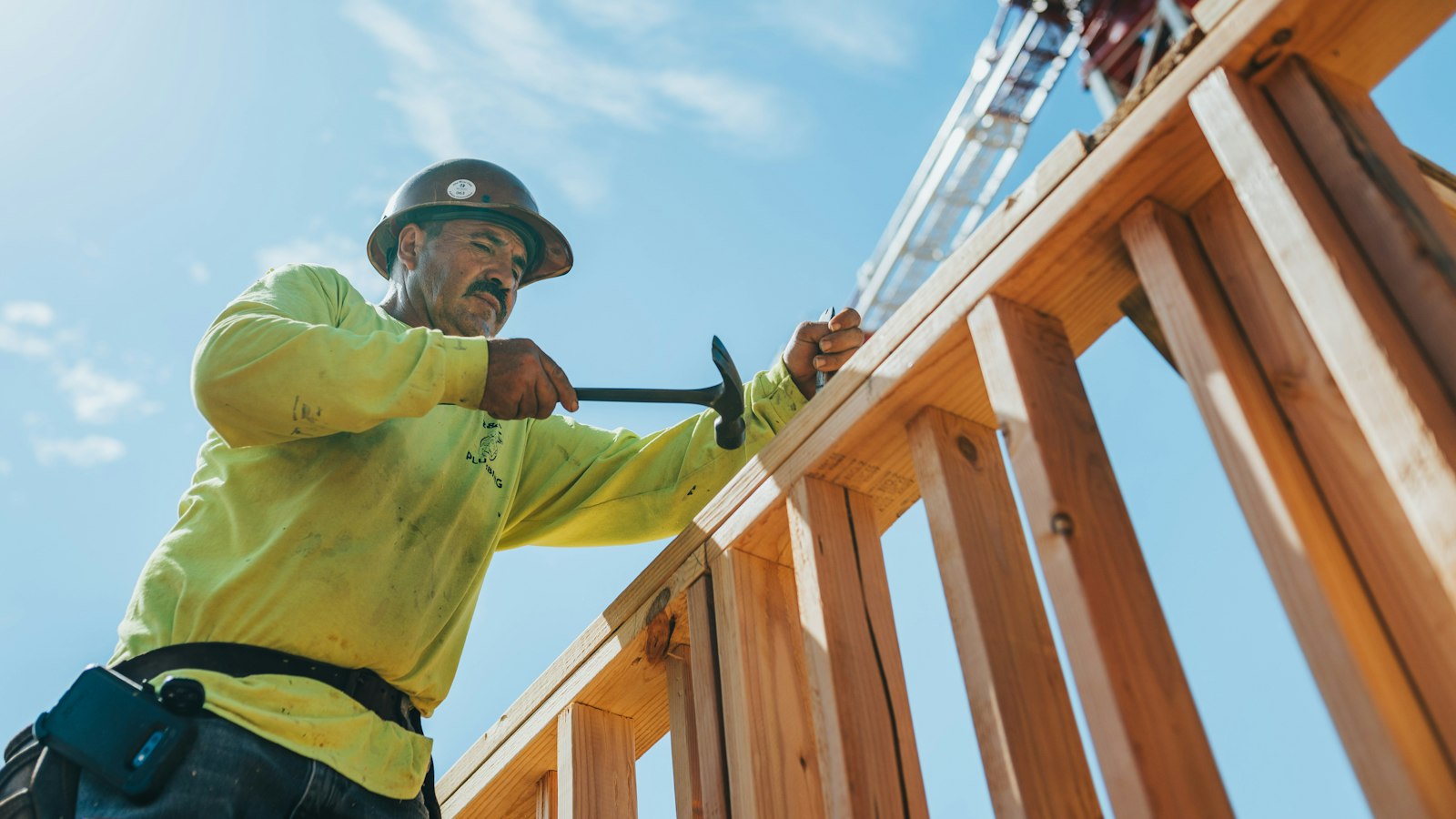 A tradesperson in a hard hat and safety gear working on a timber frame