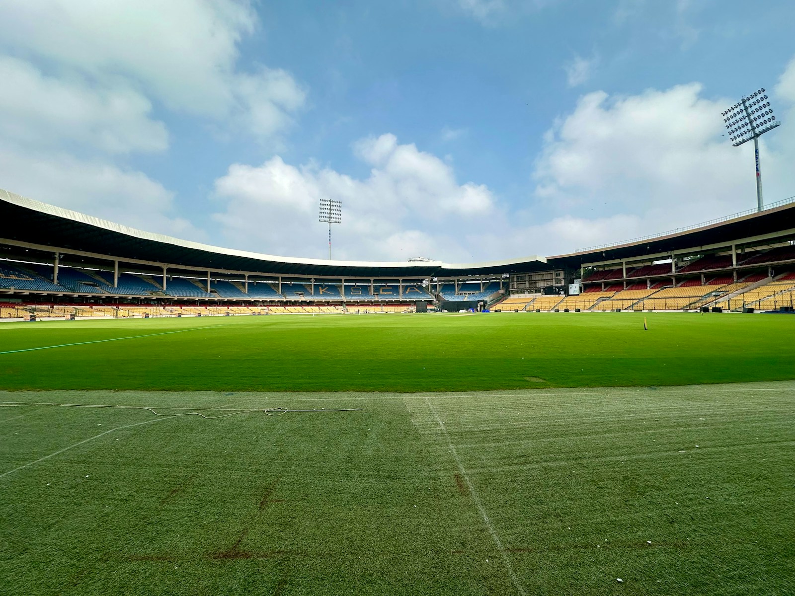 An empty green cricket ground under a blue sky.