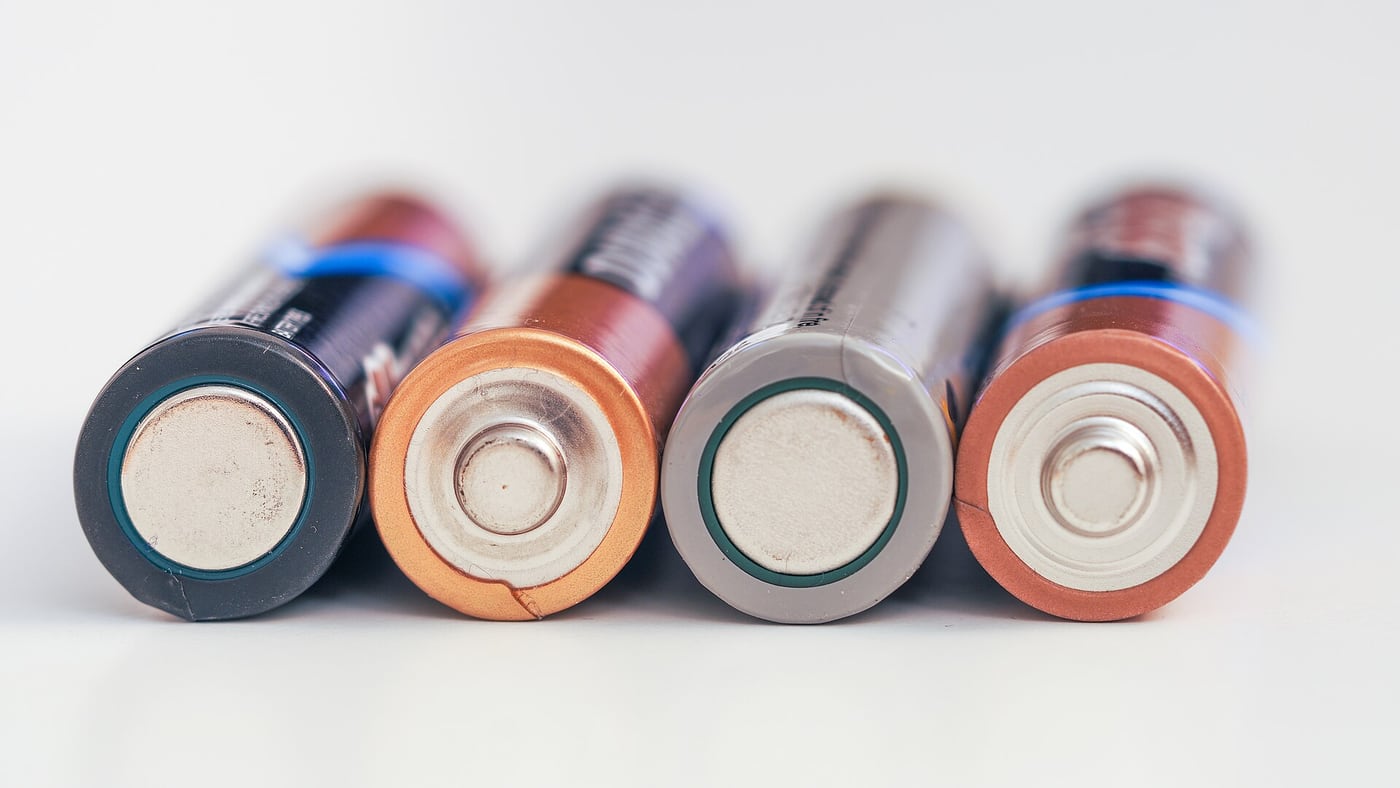 Several cylindrical AA batteries arranged on a light surface.