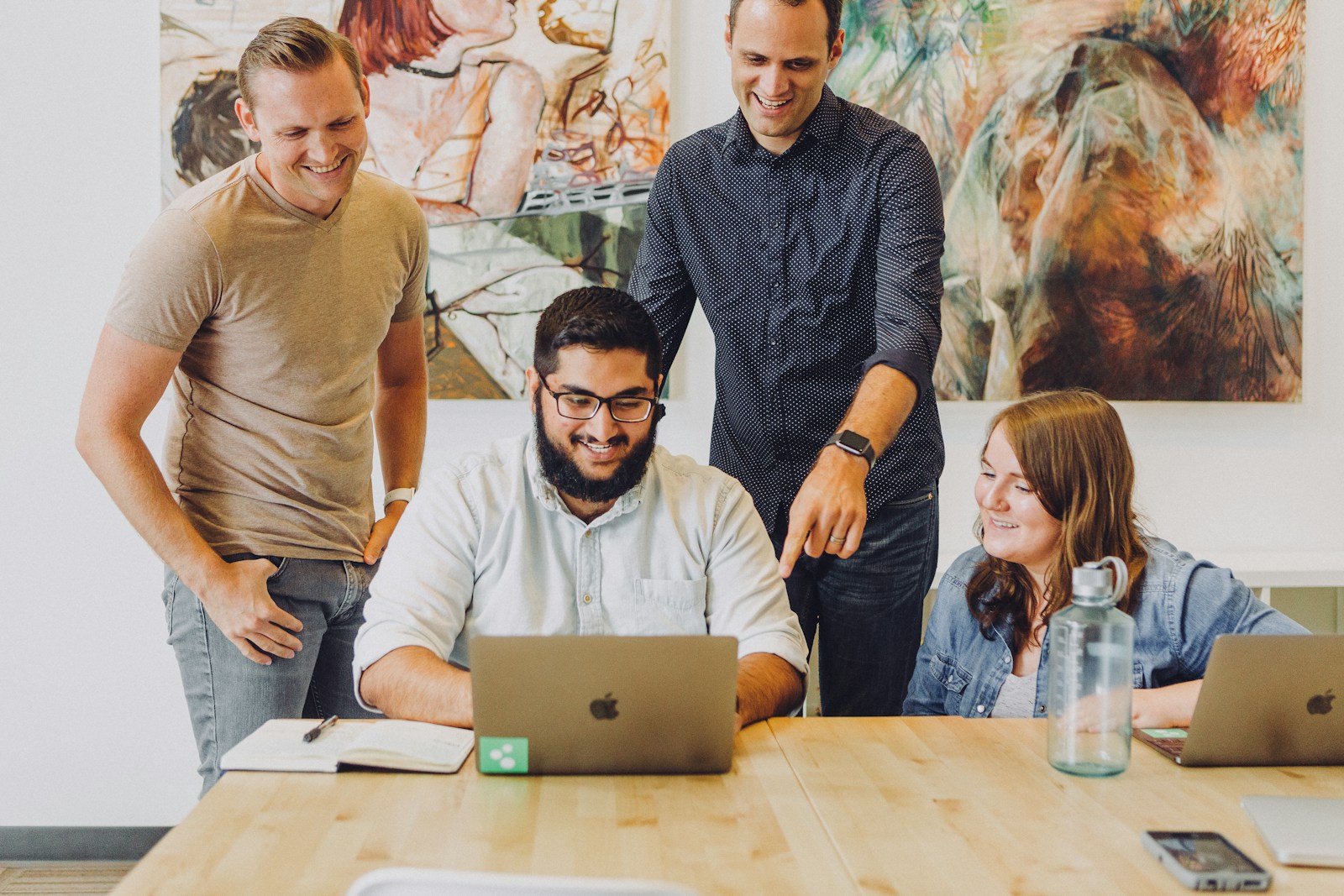 Four colleagues gathered around laptops at a table.